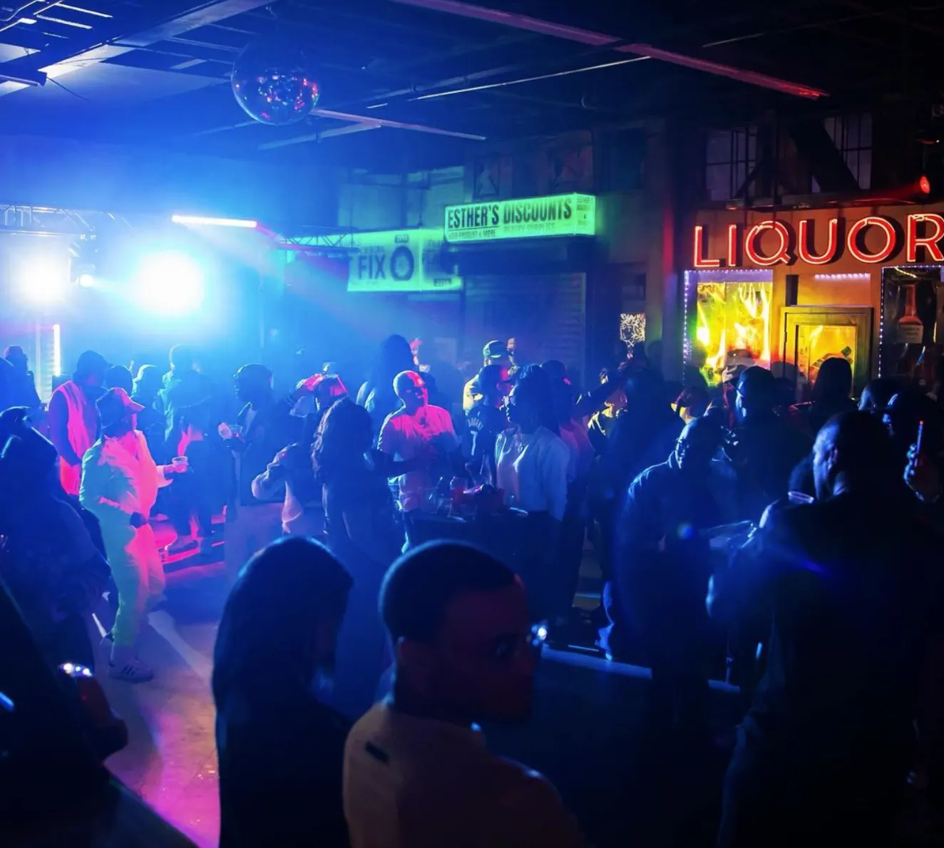 Crowded party under blue and pink lights by the Liquors sign