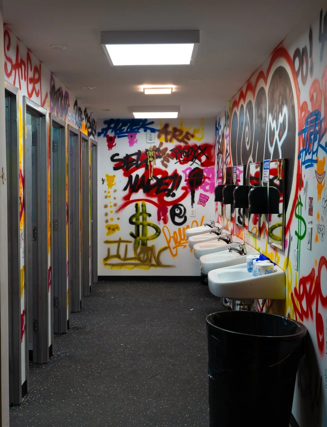 Graffiti-covered restroom with sinks and stalls