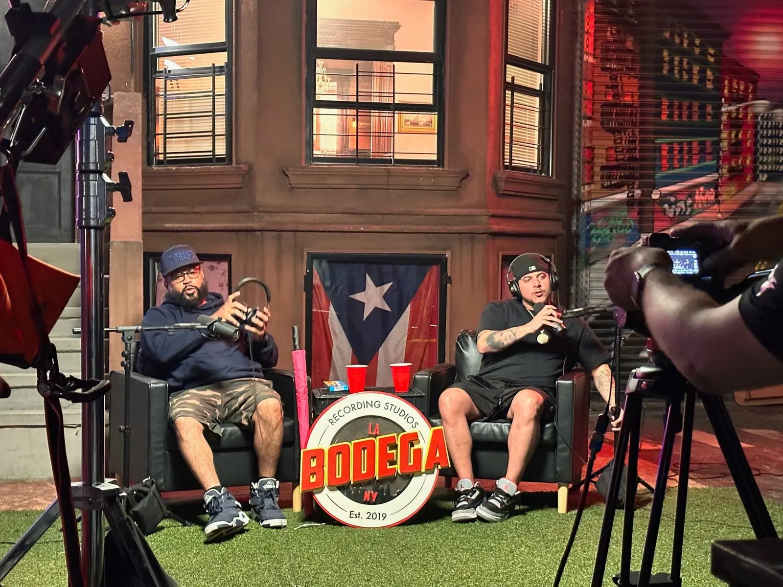 Two men seated on the brownstone stoop set with a cinema camera in frame