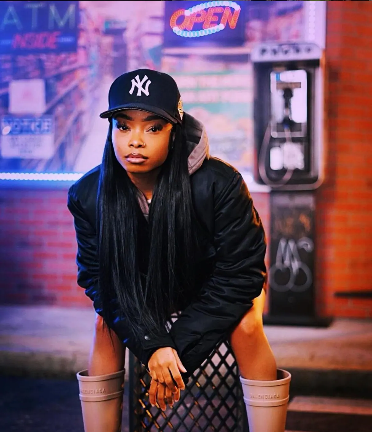 Portrait in a Yankees cap and black puffer by a payphone